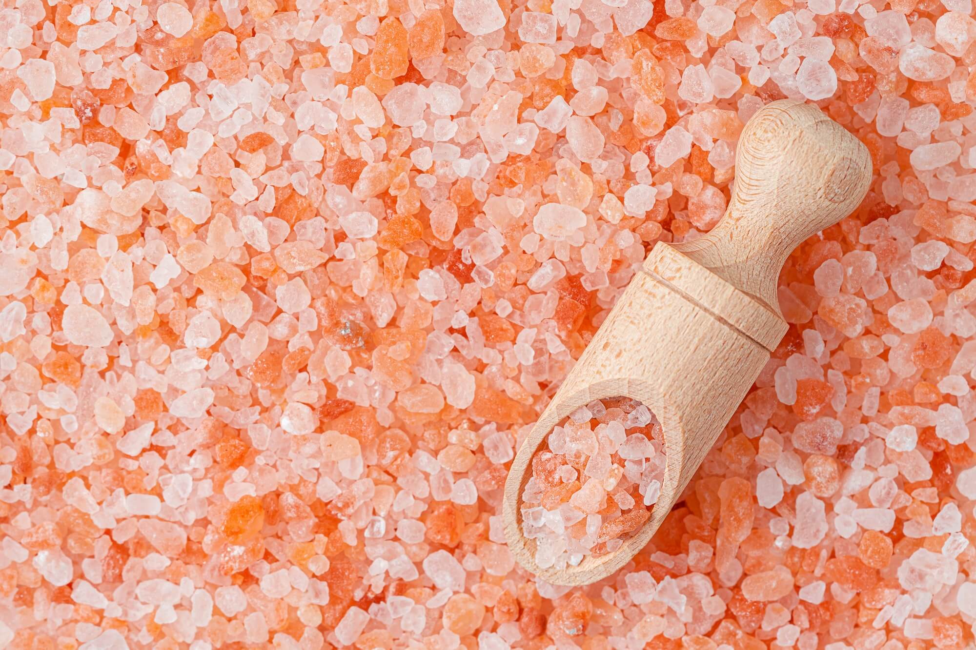 Himalayan pink salt background and wooden scoop.